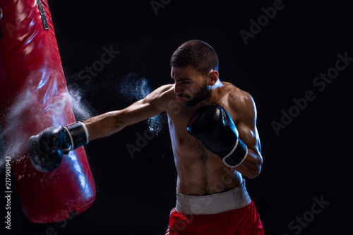 Bearded male boxer training with punching bag on black background. Male boxer as exercise for the big fight. © nazarovsergey