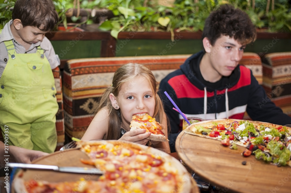 Two boys and a young girl sit in a cafe and eat a delicious large pizza