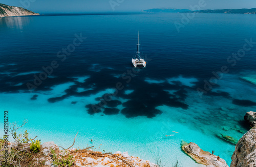Fototapeta Naklejka Na Ścianę i Meble -  White catamaran yacht at anchor in calm clear azure water lagoon. Unrecognizable tourists relax and leisure on the hidden beach