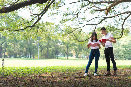 Asian student pople standing under the tree at outdoor place. Couple holding book together. Concept of education. © bixpicture