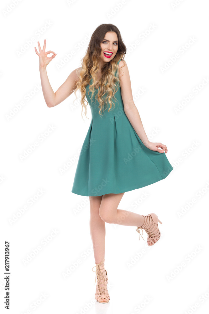 Beautiful Young Woman In Green Mini Dress And High Heels Is Showing Ok Hand Sign And Smiling Beautiful Young Woman In Green Mini Dress And High Heels Is Showing Ok Hand Sign And Smiling