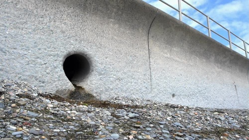 A Storm Drain Outlet set in a concrete sea wall on a shingle beach in Criccieth, Wales.