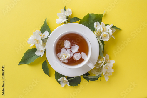 Cup of tea with petals of Jasmine flowers on a bright yellow background. Copy space,