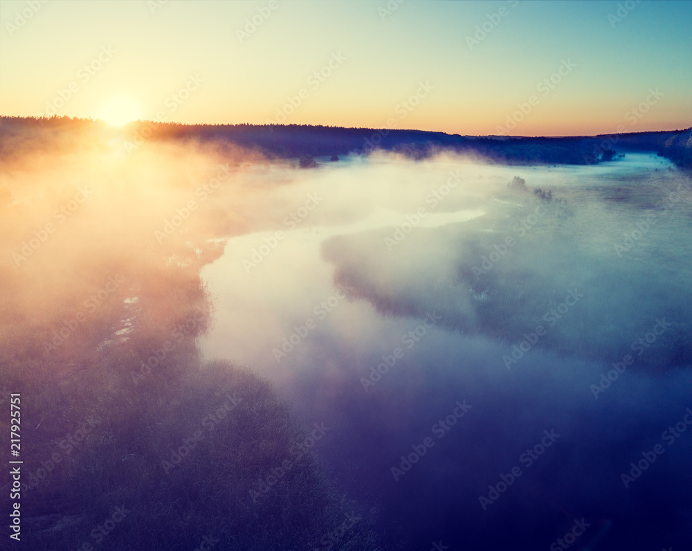 Obraz premium Early misty morning. Aerial view of countryside and river. The sun highlights the fog over the river