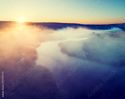 Early misty morning. Aerial view of countryside and river. The sun highlights the fog over the river