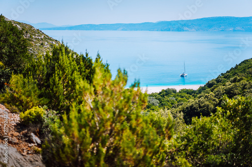 Fototapeta Naklejka Na Ścianę i Meble -  Lonely yacht on hidden Fteri beach lagoon, Kefalonia, Greece. Framed view between pine tree branches during trekking path down ravine