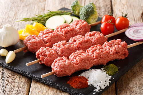 Middle Eastern Kebabs from raw minced meat on skewers with ingredients and vegetables close-up. horizontal