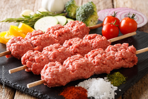 Prepared raw kebab from minced meat on skewers with ingredients and vegetables close-up. horizontal
