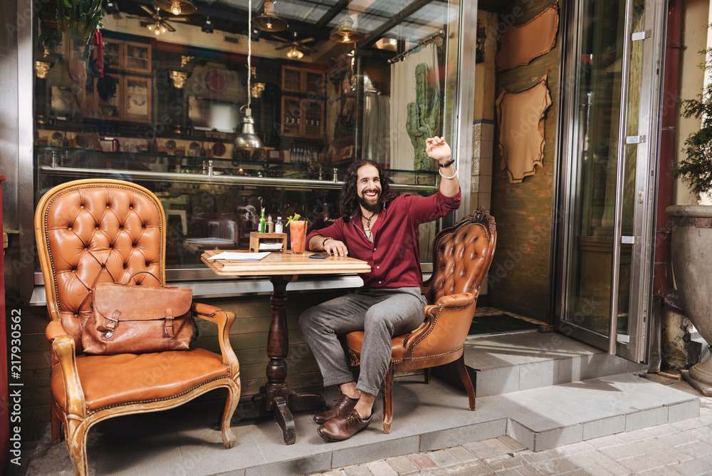 Come to me. Delighted nice man looking at the waiter while sitting at the table in the cafe