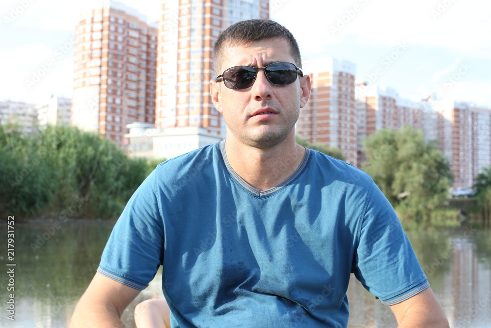 young active brunette man in sunglasses on the lake in a boat against the background of urban tall buildings