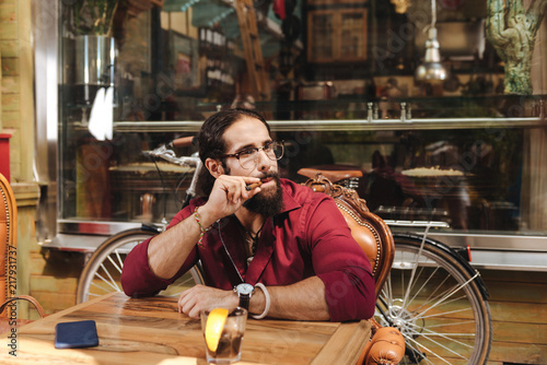 Real pleasure. Joyful happy man sitting at the table while enjoying his cigar