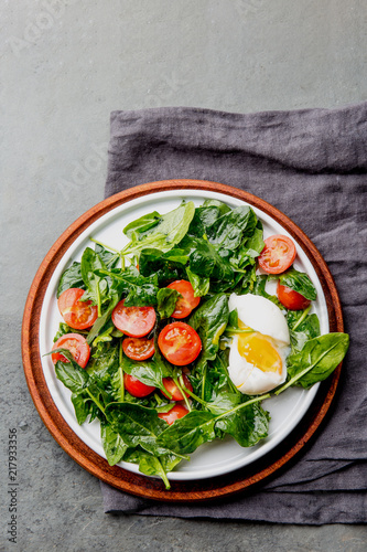 Fresh summer salad with baby spinach, tomatoes cherry and egg. Top view, copy space. Slate gray background photo