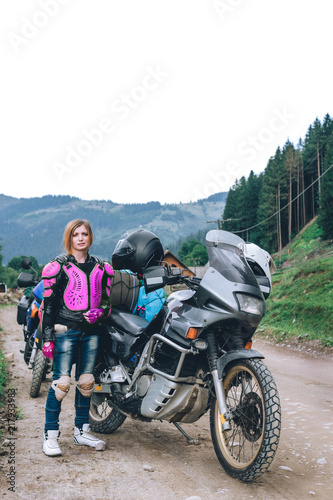A girl in pink body armor stand alone a with big adventure touring motorcycle with bags and camping equipment, off road travel jorney, traveling together, couple, mountains dirt road, vertical photo