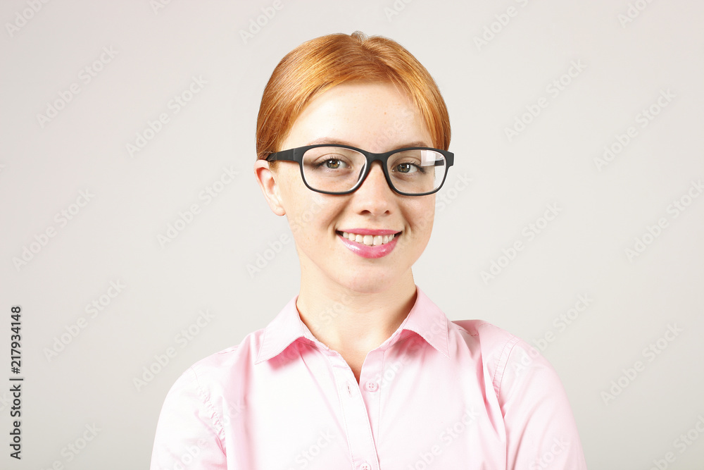 Close up portrait of beautiful young businesswoman with natural red hair wearing black frame eye glasses and pink blouse, strict formal wear dress code. Redhead female smiling. Background, copy space.