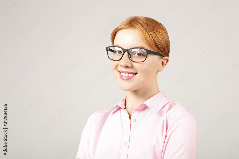 Close up portrait of beautiful young businesswoman with natural red hair wearing black frame eye glasses and pink blouse, strict formal wear dress code. Redhead female smiling. Background, copy space.