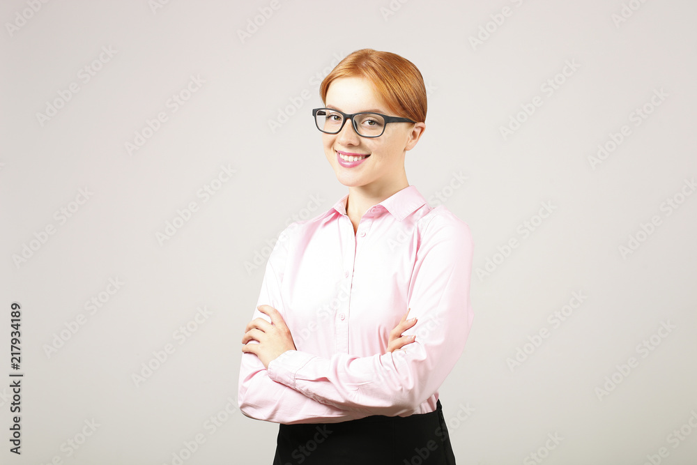 Young beautiful confident businesswoman wearing pink blouse & black frame glasses, standing w/ folded hands & smiling. Attractive redhead female with crossed arms. Background, close up, copy space. Young beautiful confident businesswoman wearing pink blouse & black frame glasses, standing w/ folded hands & smiling. Attractive redhead female with crossed arms. Background, close up, copy space.