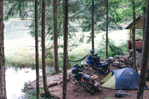 Camping in forest on side mountain lake, motorcycle touring, dual sport enduro, tent and off road adventure motorcycle, active life style concept, relax in hammock