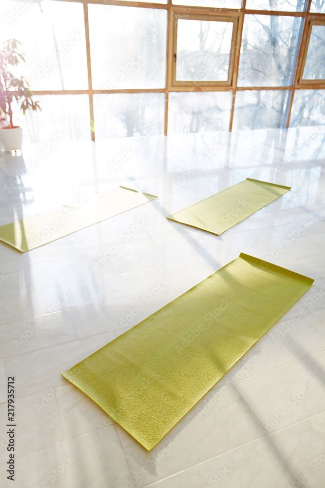 From above shot of arranged green yoga mats on white floor of light hall with sunlight shining through windows