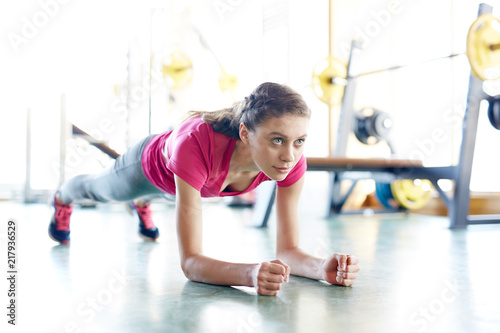 Young fit woman training in gym and doing plank exercise looking forward with determination