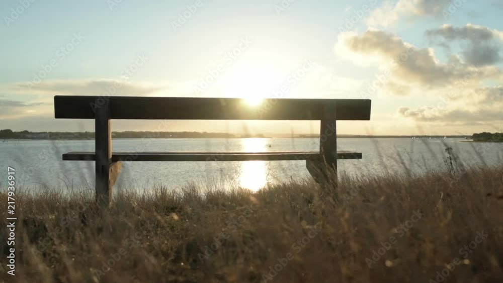 Panning past a bench at the beach with grass moving in the wind at sunrise Panning past a bench at the beach with grass moving in the wind at sunrise