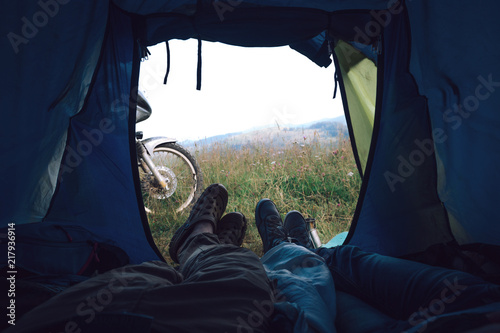 view from inside a tent at the mountain and legs of two people emerge from tent. travel and motorcycle road trip concept. Tourist tent outside