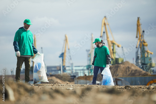 Two volunteers men in green uniform working and collecting rubbish on construction site