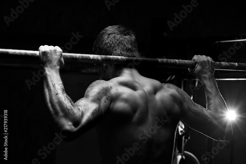 Strong young man doing pull up exercise on horizontal bar in gym. Sports, fitness, gymnastics workout.