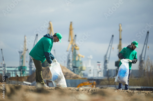Two volunteers in green uniform picking garbage on construction site