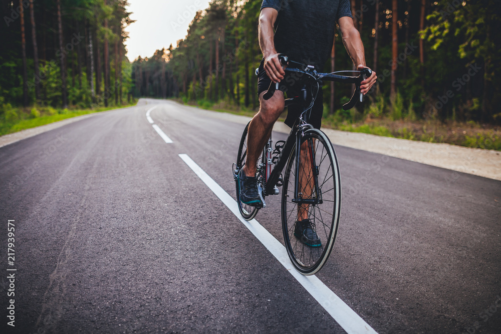 Road bike cyclist, man cycling on empty road in sunset	