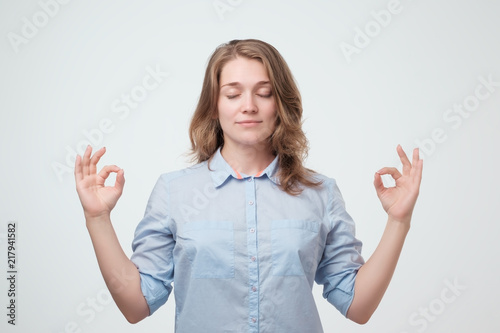 Restful peaceful female feels relaxed in blue shirt, stands near gray wall, tries to concentrate or to be focused photo