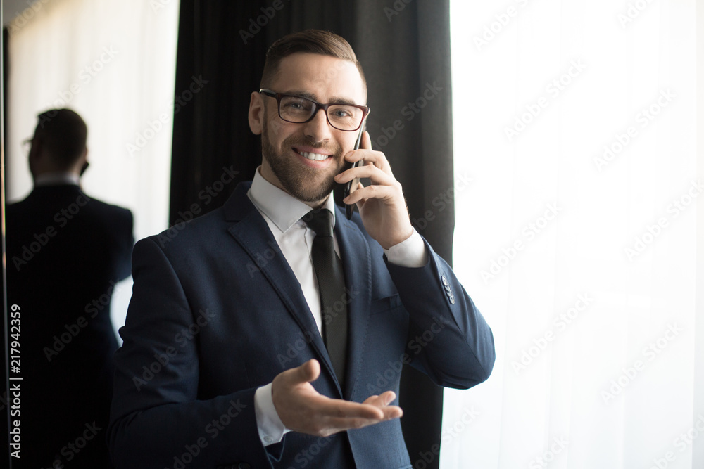 Handsome stylish businessman in glasses speaking on phone cheerfully and smiling at camera Handsome stylish businessman in glasses speaking on phone cheerfully and smiling at camera