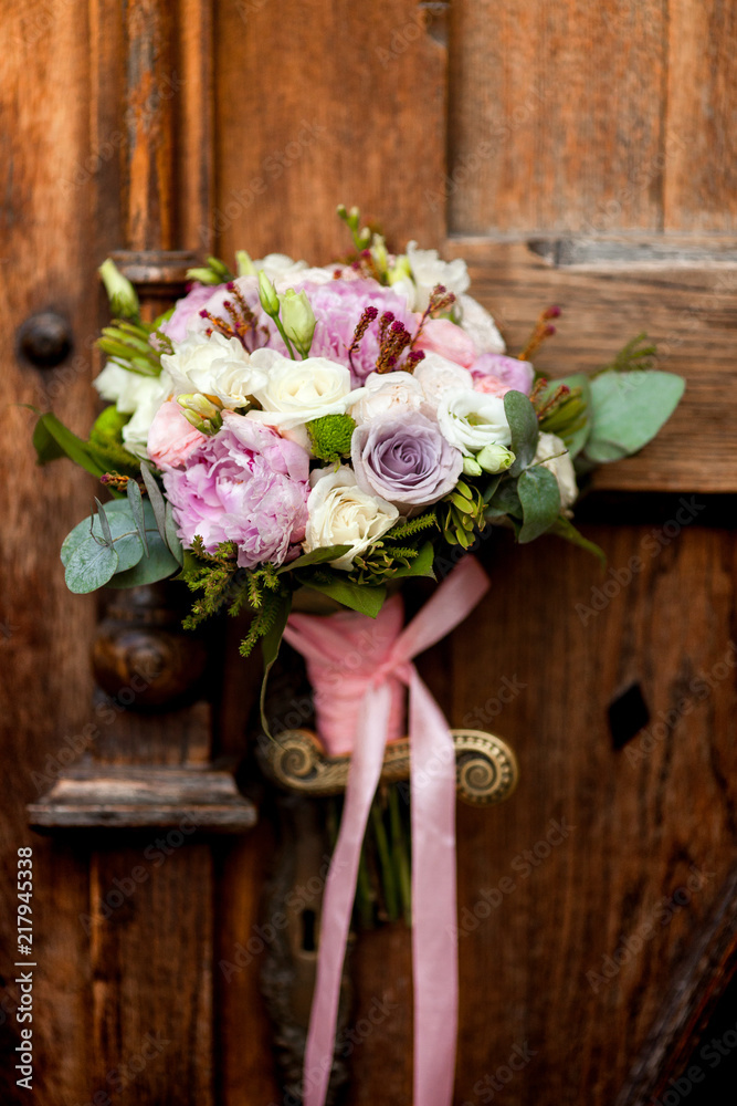 Wedding bouquet hanging on an old door handle on the background of ancient wooden doors. Wedding bouquet hanging on an old door handle on the background of ancient wooden doors.