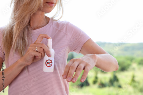 Mosquito repellent. Woman using insect repellent spray outdoors. photo