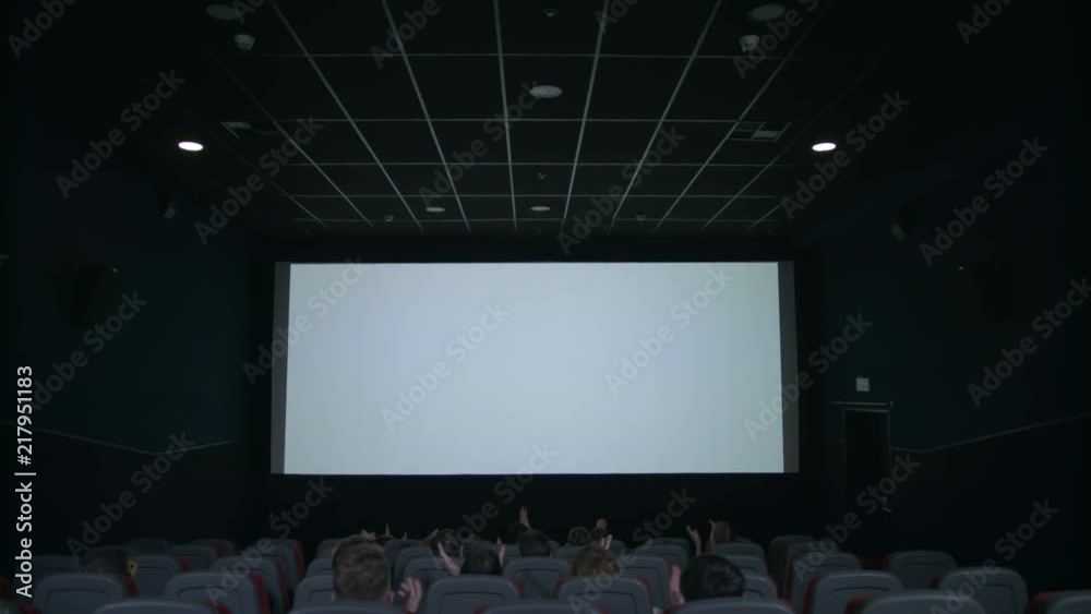 Spectators sitting in front of white screen in cinema. Spectator looking on cinema white screen. People applauding in front of cinema screen in movie theatre