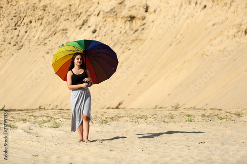 Piękna dziewczyna z kolorowym parasolem na piaszczystej wydmie.