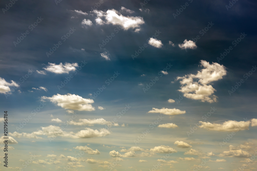 Vibrant dark blue sky with white to yellow clouds. Beautiful moody nature background