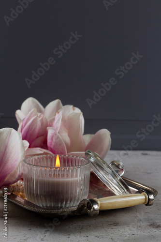 burning candle and magnolia fresh flowers on tray close up, low key