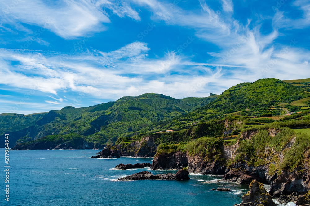 The coast line of Flores island in Azores, green landscape with blue sky and some Clouds