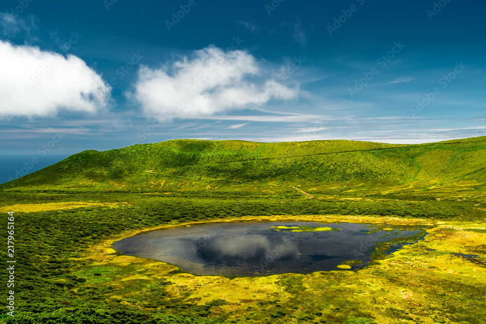 A blue lagoon in Flores island Azores, with a green mountain and a blue sky with some clouds