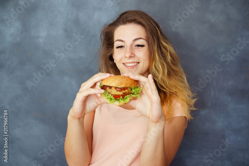 Fast-food, diet, self-control, appetite, satisfaction, delight, unhealthy eating. Young cute woman with hamburger in hands enjoying food