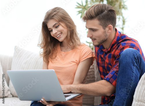 Wallpaper Mural young couple is using a laptop and smiling while sitting on sofa at home Torontodigital.ca