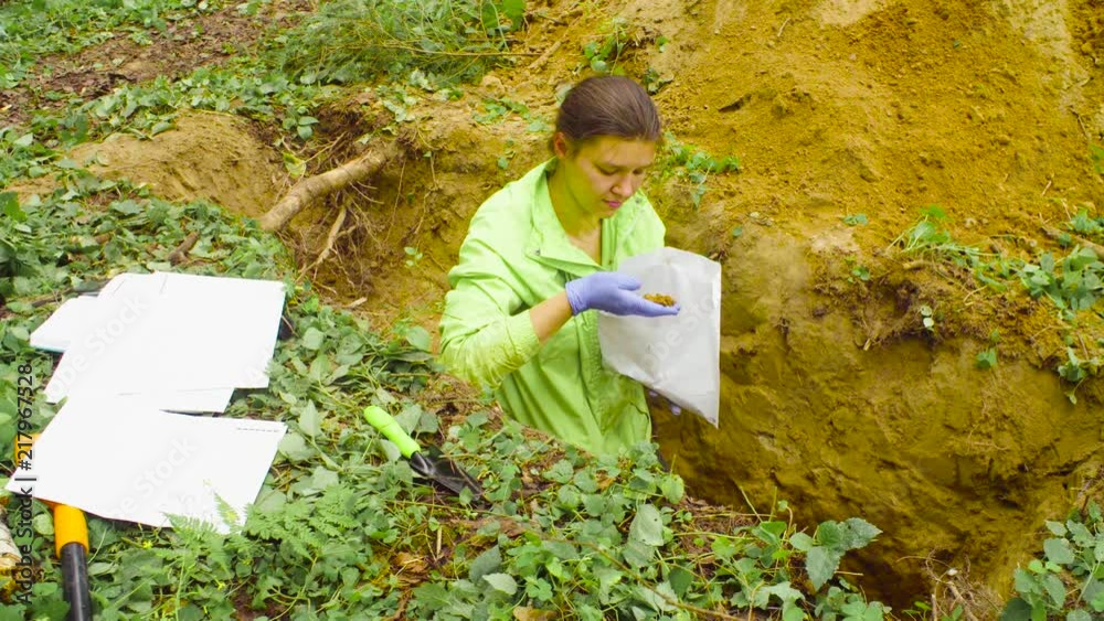 Woman scientist environmentalist taking samples of a soil and putting them into the paper envelope