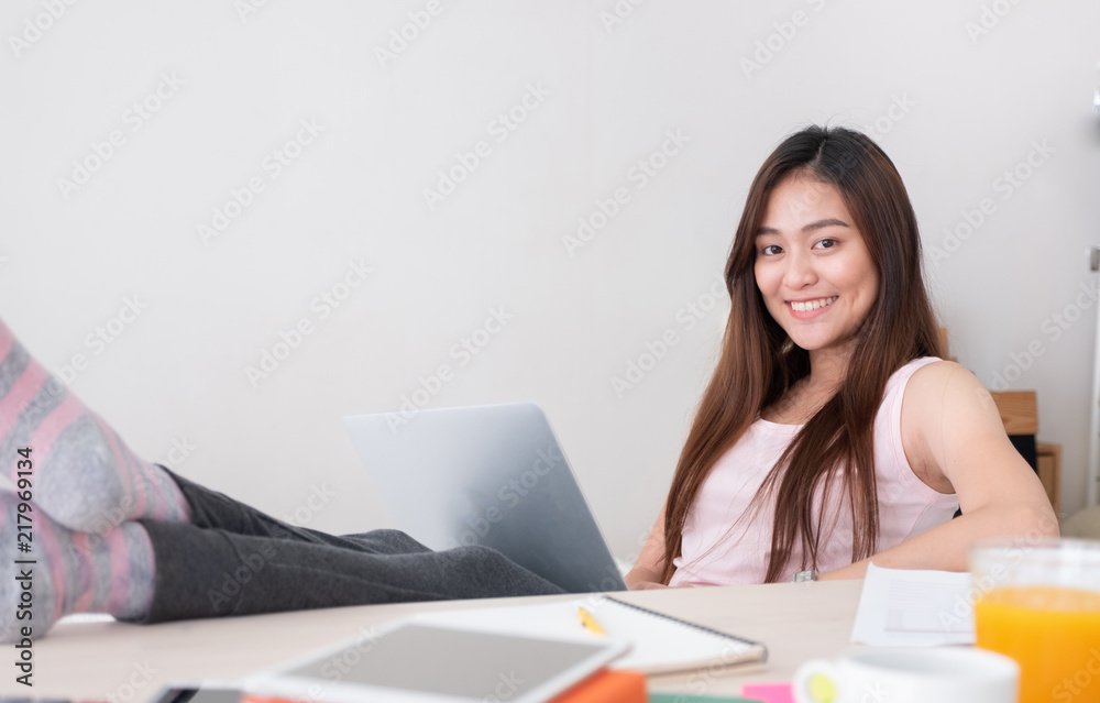 Asian female freelancer smile and holding laptop with rest leg on table in bedroom at home.Work at home concept.work from home concept. Asian female freelancer smile and holding laptop with rest leg on table in bedroom at home.Work at home concept.work from home concept.