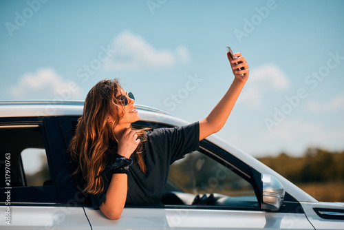 Woman taking selfie while leaning on car window. © chika_milan