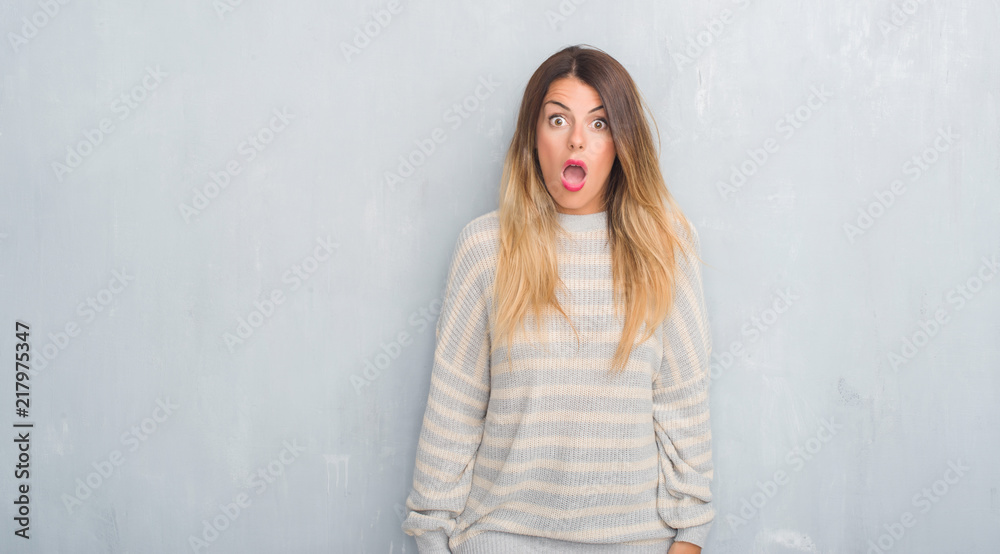 Fototapeta premium Young adult woman over grunge grey wall wearing winter sweater afraid and shocked with surprise expression, fear and excited face.