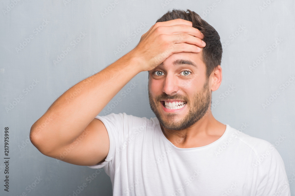 Handsome young man over grey grunge wall stressed with hand on head, shocked with shame and surprise face, angry and frustrated. Fear and upset for mistake. Handsome young man over grey grunge wall stressed with hand on head, shocked with shame and surprise face, angry and frustrated. Fear and upset for mistake.