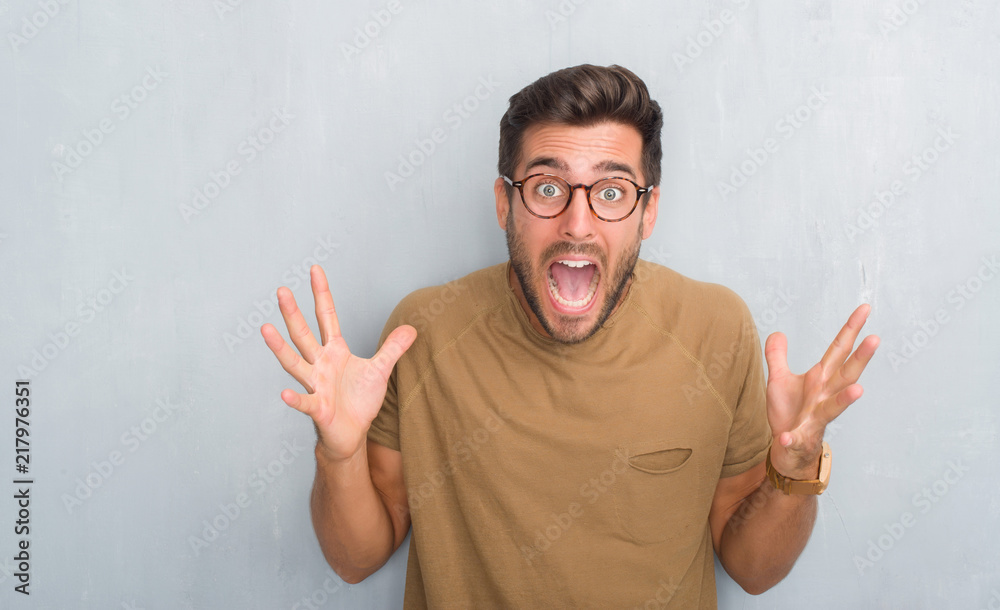 Handsome young man over grey grunge wall wearing glasses celebrating crazy and amazed for success with arms raised and open eyes screaming excited. Winner concept Handsome young man over grey grunge wall wearing glasses celebrating crazy and amazed for success with arms raised and open eyes screaming excited. Winner concept
