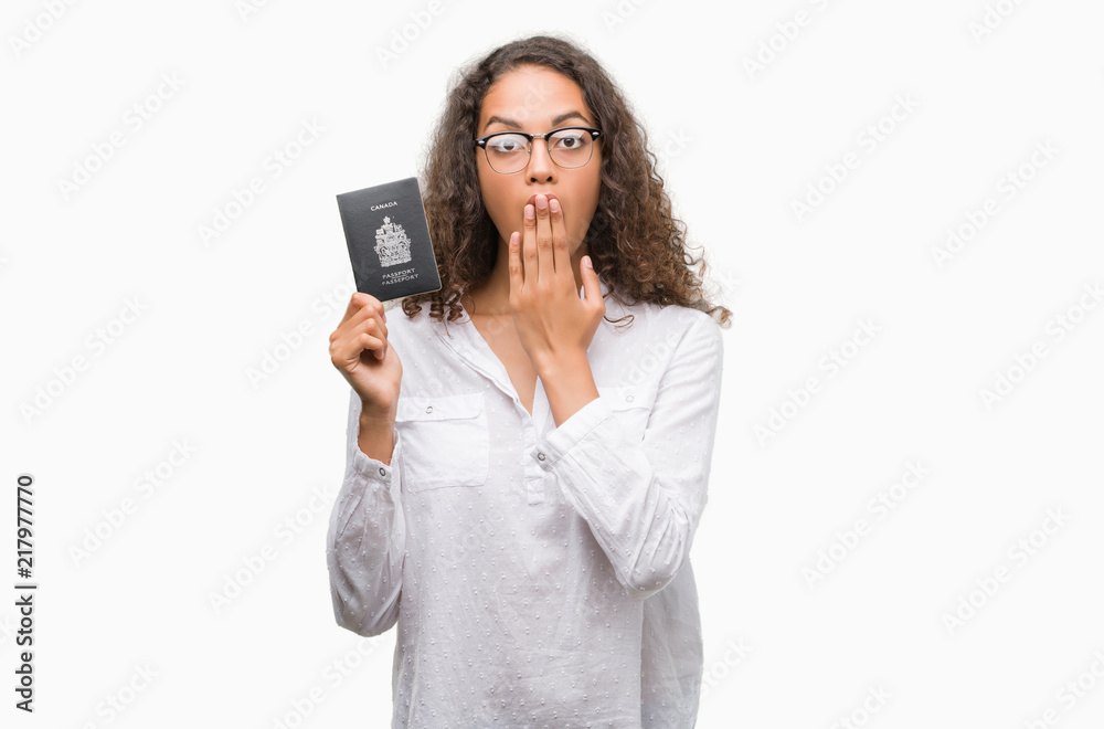 Young hispanic woman holding passport of Canada cover mouth with hand shocked with shame for mistake, expression of fear, scared in silence, secret concept Young hispanic woman holding passport of Canada cover mouth with hand shocked with shame for mistake, expression of fear, scared in silence, secret concept