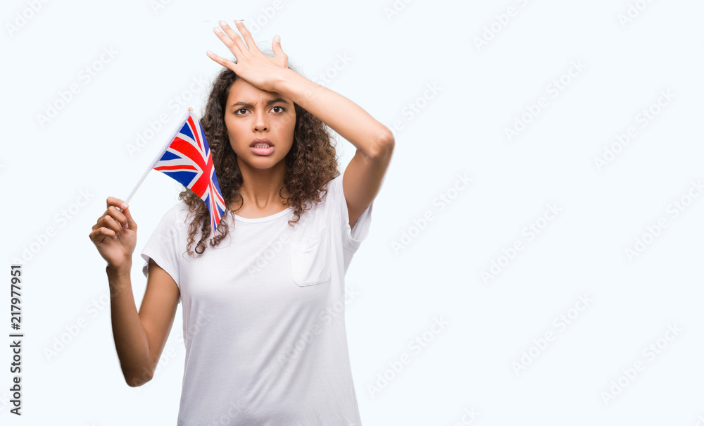 Young hispanic woman holding flag of United Kingdom stressed with hand on head, shocked with shame and surprise face, angry and frustrated. Fear and upset for mistake.
