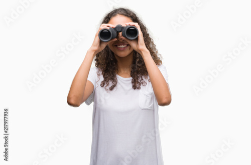 Young hispanic woman looking through binoculars with a happy face standing and smiling with a confident smile showing teeth